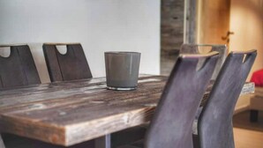 Une table à manger en bois, avec quatre chaises, un verre posé sur la table, et un mur rustique en arrière-plan.