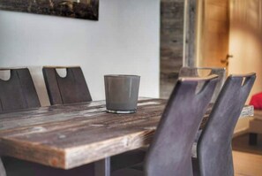 Uma mesa de jantar de madeira com quatro cadeiras, um copo sobre a mesa, e uma parede rústica ao fundo.