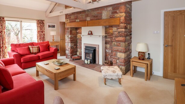 A living room with a red sofa, a wooden coffee table, a fireplace, and a brick wall. - Edencroft (Penrith)