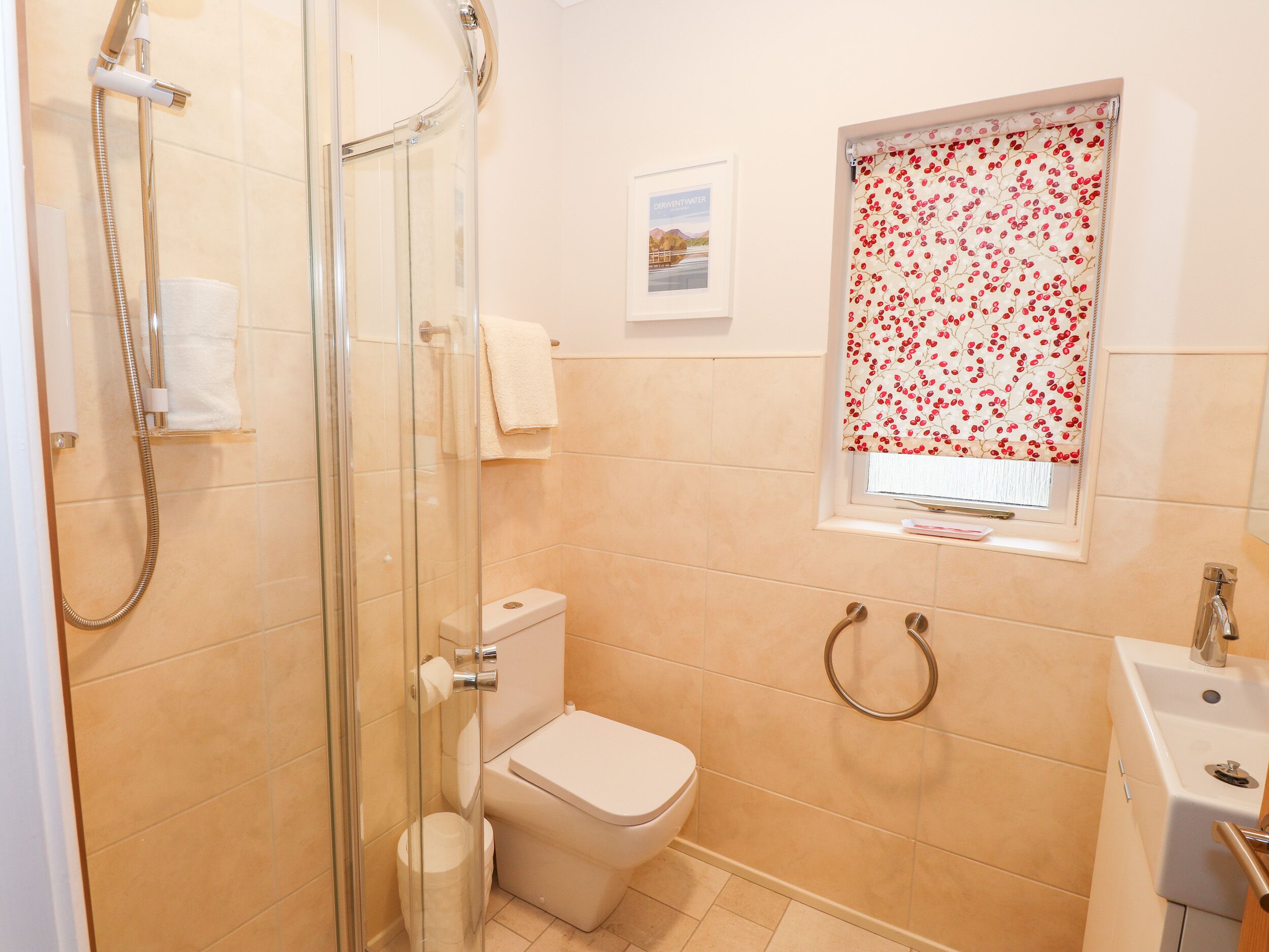 A bathroom with a glass-enclosed shower, a toilet, a sink, and a window with a floral curtain.