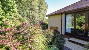 A house with a garden, a wooden bench, and a large window. - Edencroft (Penrith)