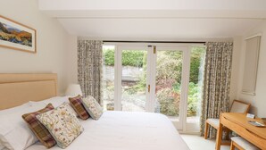 A bedroom with a large bed, a desk, and a view of a garden through a sliding door. - Edencroft (Penrith)