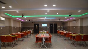 A spacious dining area with multiple tables and chairs, ceiling fans, and recessed lighting. - Hotel Kiran (Haridwar)