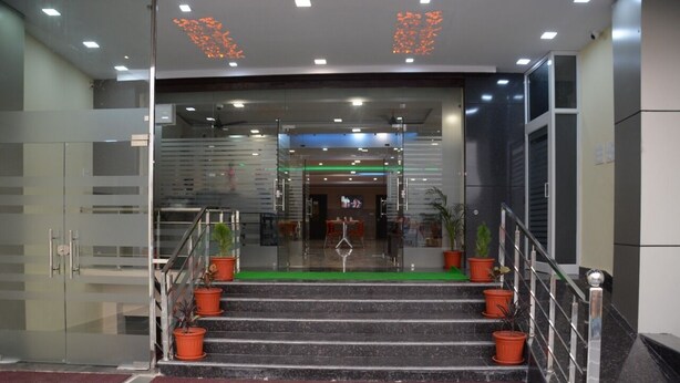 A modern hotel lobby with a staircase leading to the entrance, glass walls, and potted plants. - Hotel Kiran (Haridwar)
