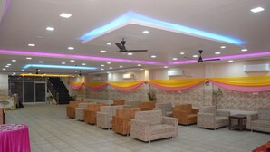 A spacious hall with rows of sofas and chairs, air conditioning units, and a staircase in the background. - Hotel Kiran (Haridwar)