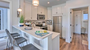 A modern kitchen with white cabinets, stainless steel appliances, and a central island with bar stools. - Traverse City Townhome: Walk to Beach! (Traverse City)