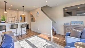 A modern kitchen with bar stools, a staircase, and a living area with a sofa and a coffee table. - Traverse City Townhome: Walk to Beach! (Traverse City)