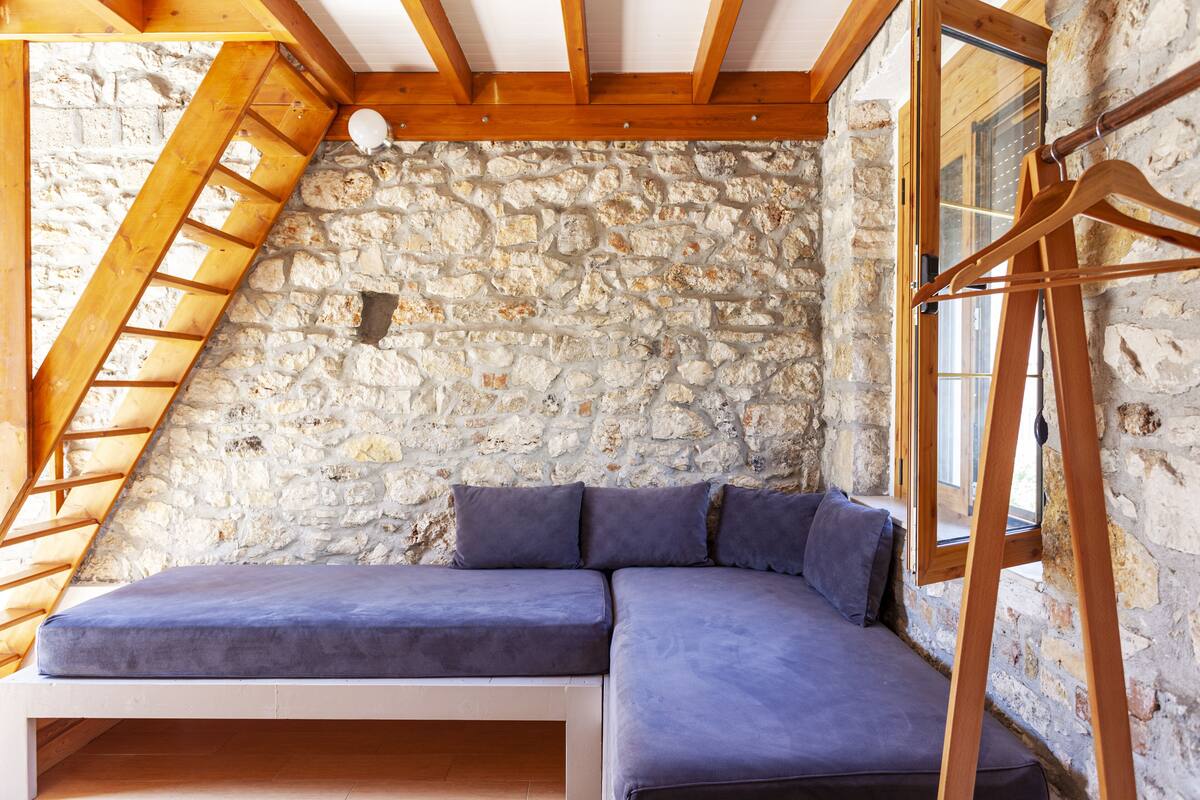 A loft bedroom with a stone wall, wooden beams, a built-in bench, and a wooden hanger.