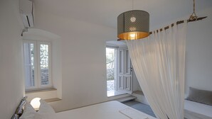 A bedroom with a bed, a bedside table, a hanging light fixture, and a view of the outside through a window. - Militiko Residence (Himarë)