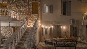 A stone staircase with white balustrades leading to a second floor. There is a table with chairs and a small potted plant in the foreground. - Militiko Residence (Himarë)