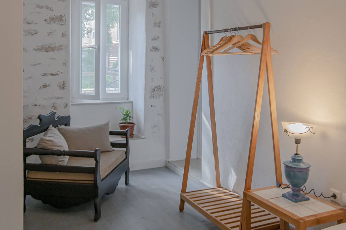 A bedroom with a bed, a wooden wardrobe, a bedside table with a lamp, and a window.