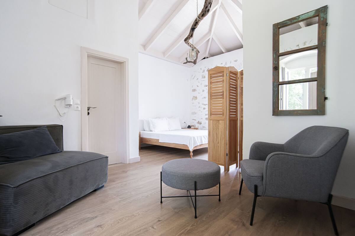 A modern bedroom with a bed, a grey sofa, a grey armchair, and a wooden wardrobe.