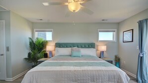 A bedroom with a large bed, two bedside lamps, a ceiling fan, and a window with curtains. - Knot Salty: Ocean-view 4-bedroom for up to 11 in North Topsail Beach. (North Topsail Beach)