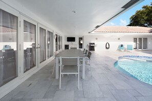 Un espace extérieur abrité comprenant une piscine, une table à manger avec des chaises et un barbecue.