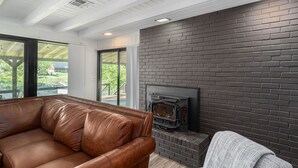 A modern living room with a leather sofa, a fireplace, and a view of greenery outside. - 2Kings 2Doubles - Boat Dock in Cozy Cove PetsAsk (Mead)