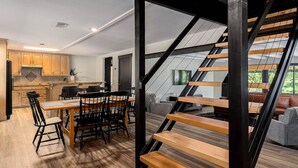 A modern kitchen with wooden cabinets, a dining area with a wooden table and chairs, and a staircase with wooden steps. - 2Kings 2Doubles - Boat Dock in Cozy Cove PetsAsk (Mead)