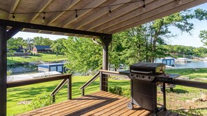 A wooden deck with a barbecue grill, overlooking a grassy area and a body of water. - 2Kings 2Doubles - Boat Dock in Cozy Cove PetsAsk (Mead)