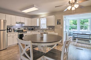 A modern kitchen with white cabinetry, a central island, and a dining area with a bench. - Coastal Escape w/ Water Access & Sunroom (Ocean View)