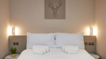 A neatly made bed with white linens, two bedside lamps, and a wall-mounted artwork of a deer head.