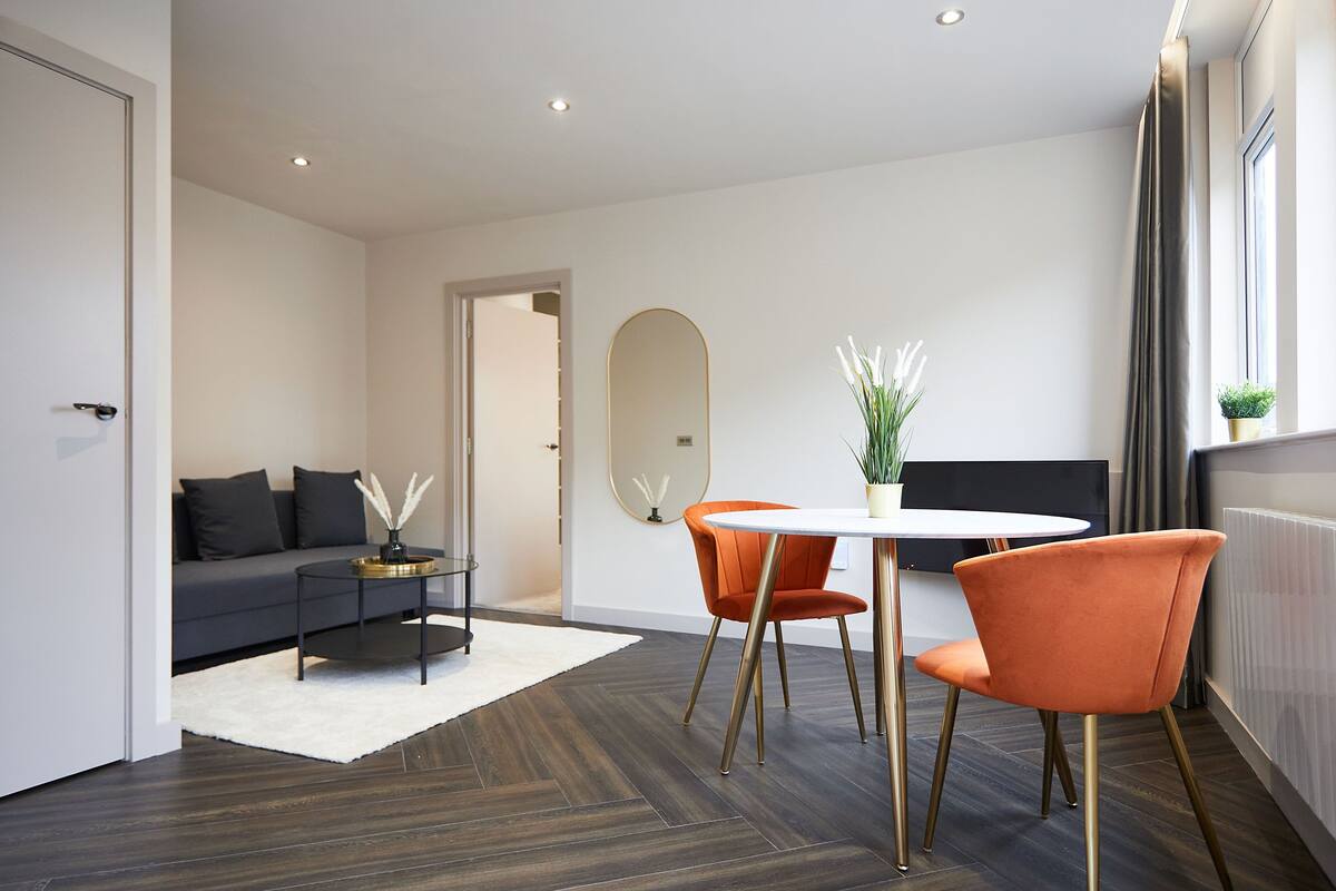 A modern living room with a sofa, a round table, and two orange chairs.