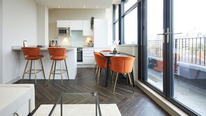 Une cuisine moderne avec des meubles blancs, un four à micro-ondes en acier inoxydable et un coin repas avec des chaises orange et une table noire.