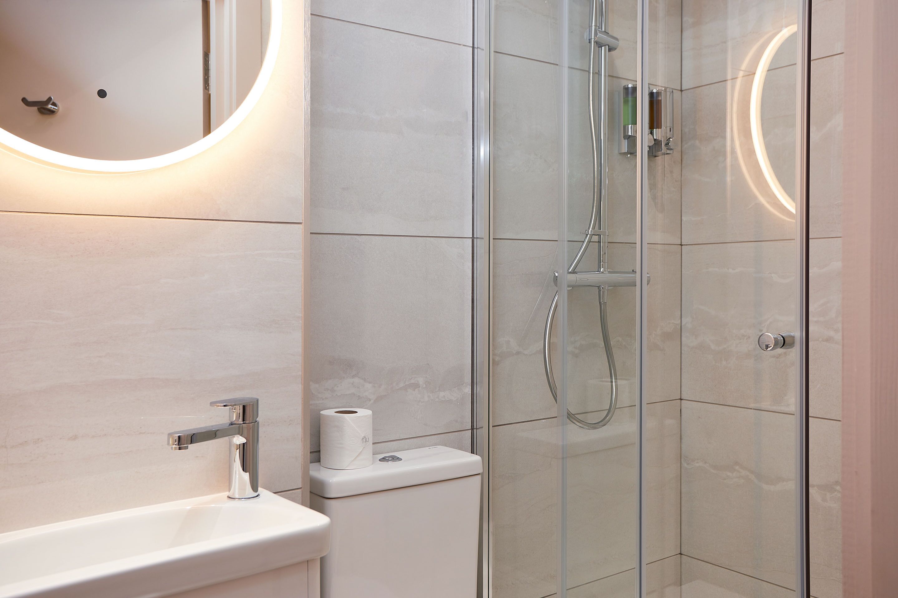 Een moderne badkamer met een douche met glazen wand, een wastafel met spiegel en een toilet.