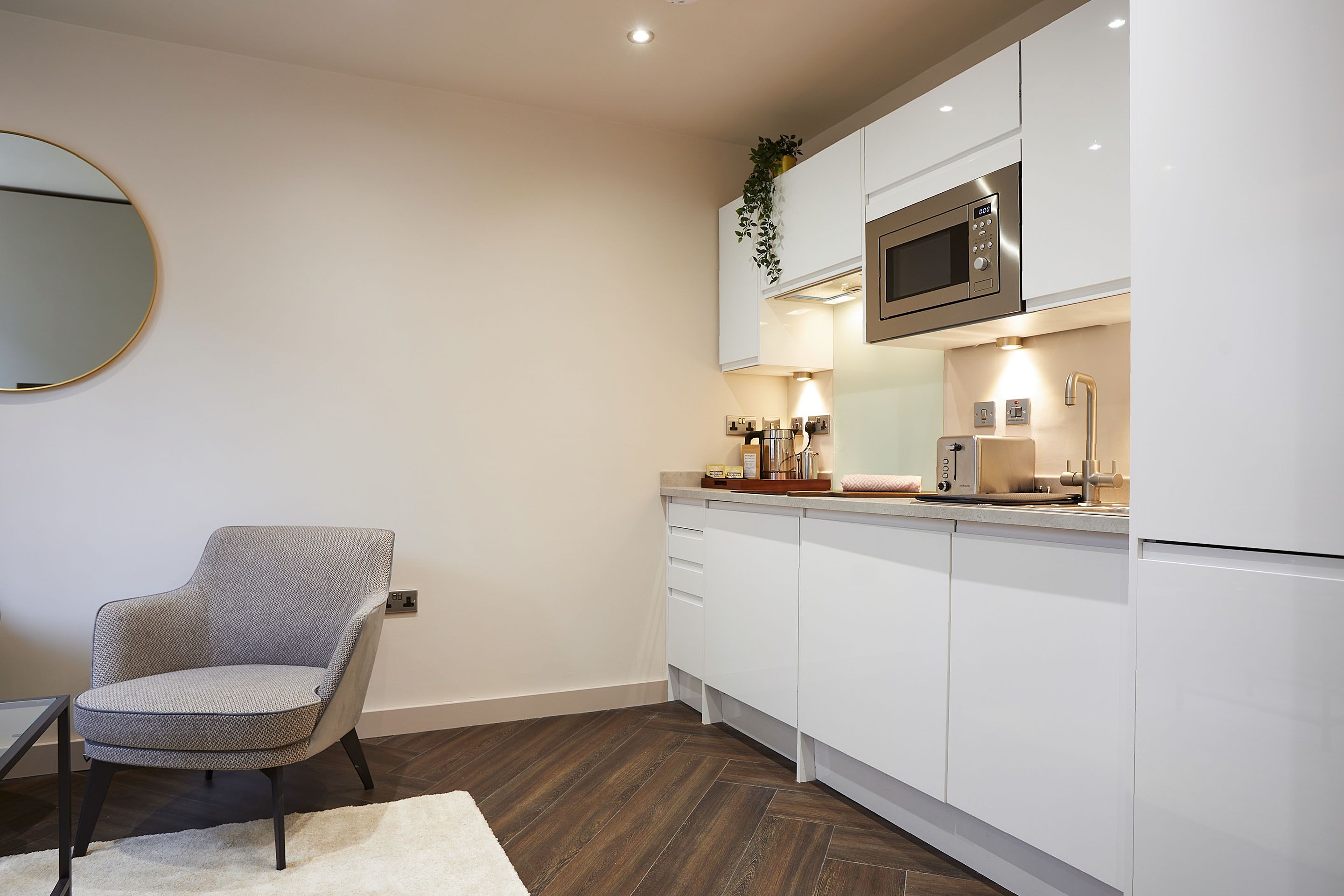 A modern kitchen with white cabinets, a microwave, and a sink. There is a chair and a small table with a rug.