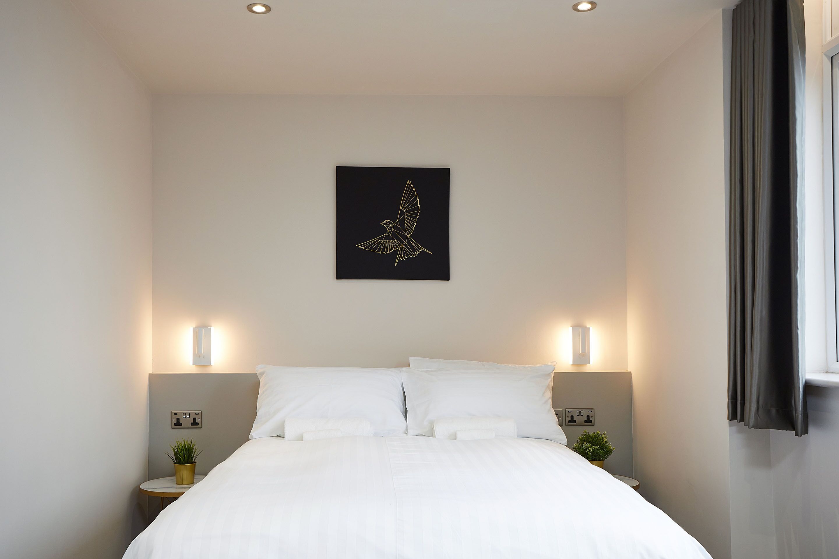 A neatly made bed with white linens, two bedside tables with lamps, and a wall-mounted artwork of a bird.