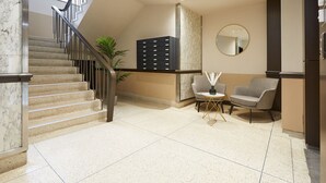 Un hall d’entrée spacieux avec un escalier en marbre, un coin salon comprenant deux fauteuils, une petite table et un grand miroir mural.