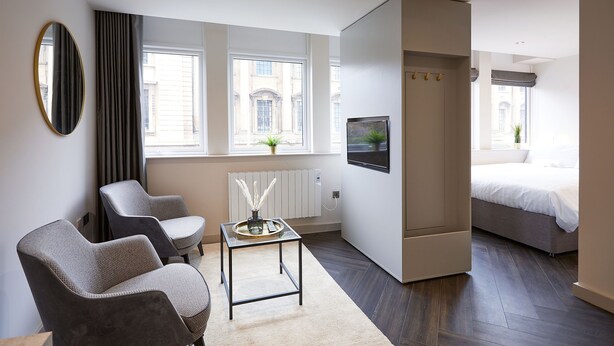 Une chambre d’hôtel moderne équipée d’un lit, de deux fauteuils, d’une petite table, d’un téléviseur et de grandes fenêtres.
