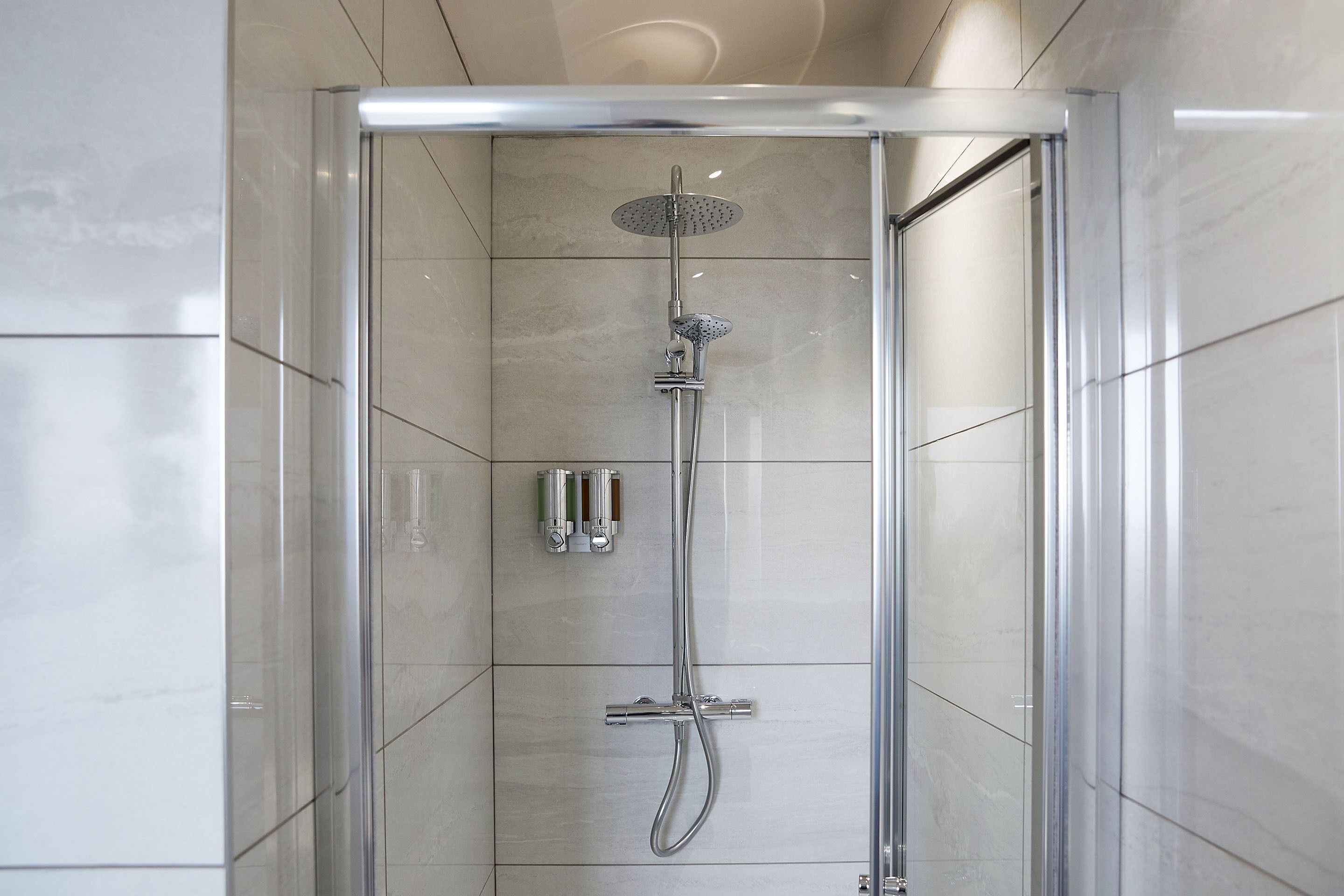 Une cabine de douche moderne dotée d’une porte en verre, de robinetterie chromée et d’un sol carrelé.