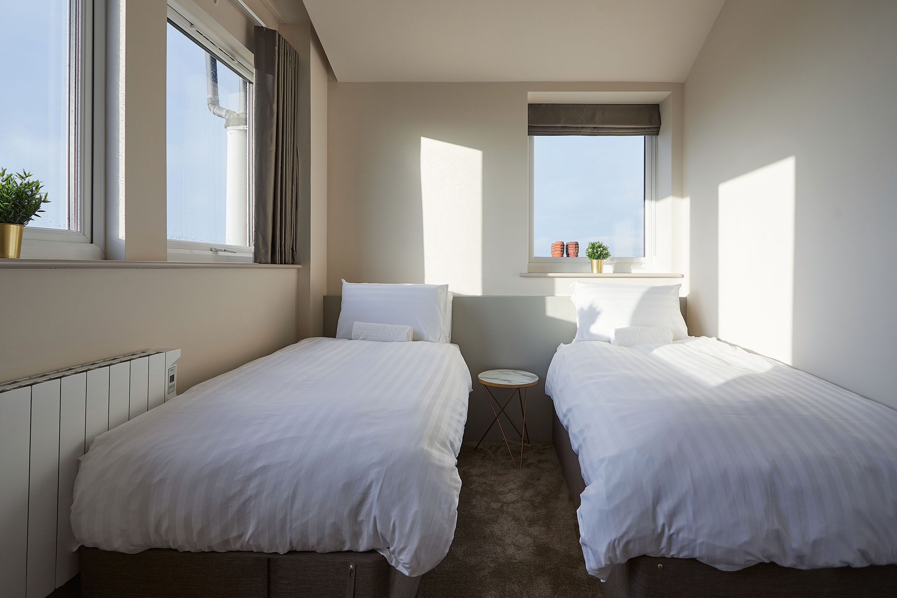 Un dormitorio con dos camas, una mesita redonda y un ventanal con vistas.