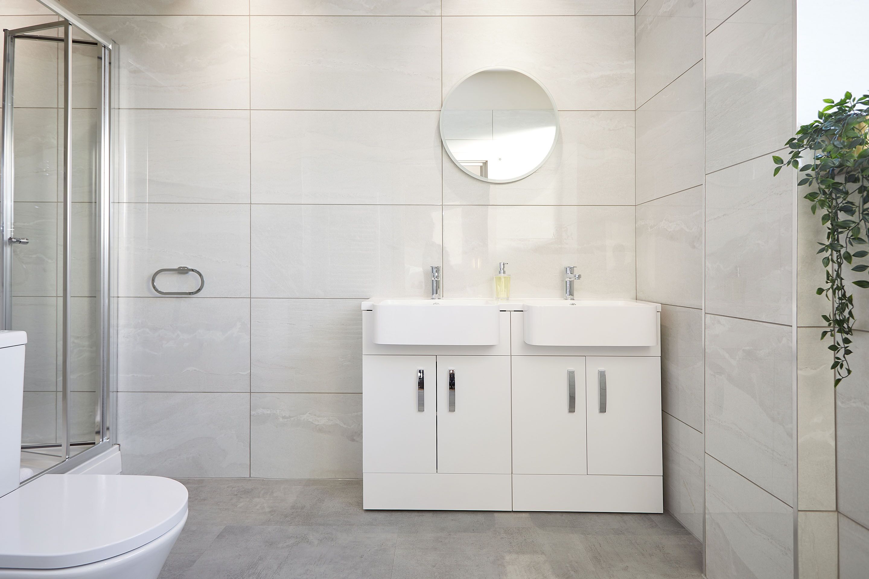 Ein modernes Badezimmer mit Toilette, einer Duschkabine und einem Waschtisch mit zwei Waschbecken und einem Spiegel.