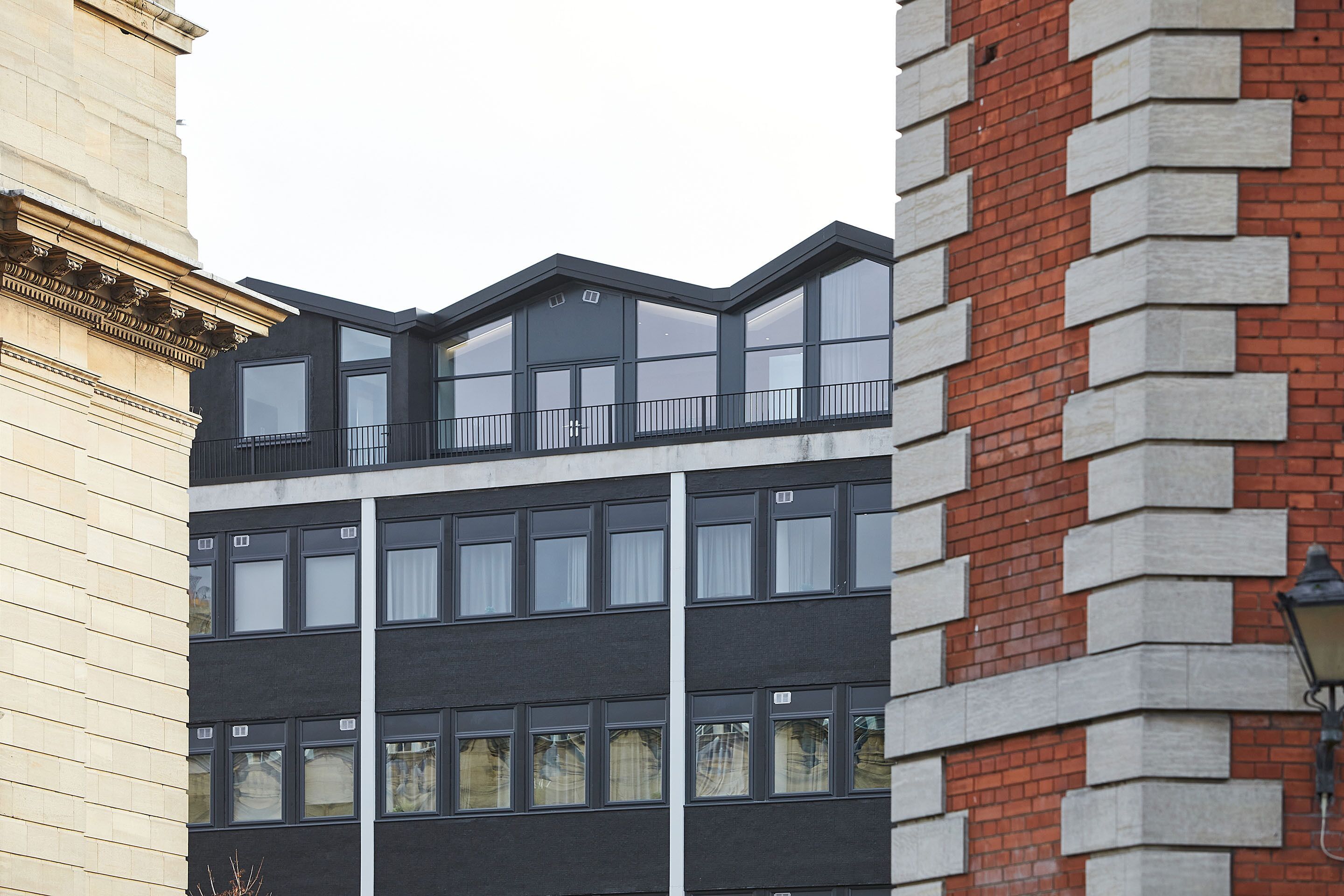 Un edificio moderno con fachada negra, ventanas amplias y una sección de ladrillo a la derecha.
