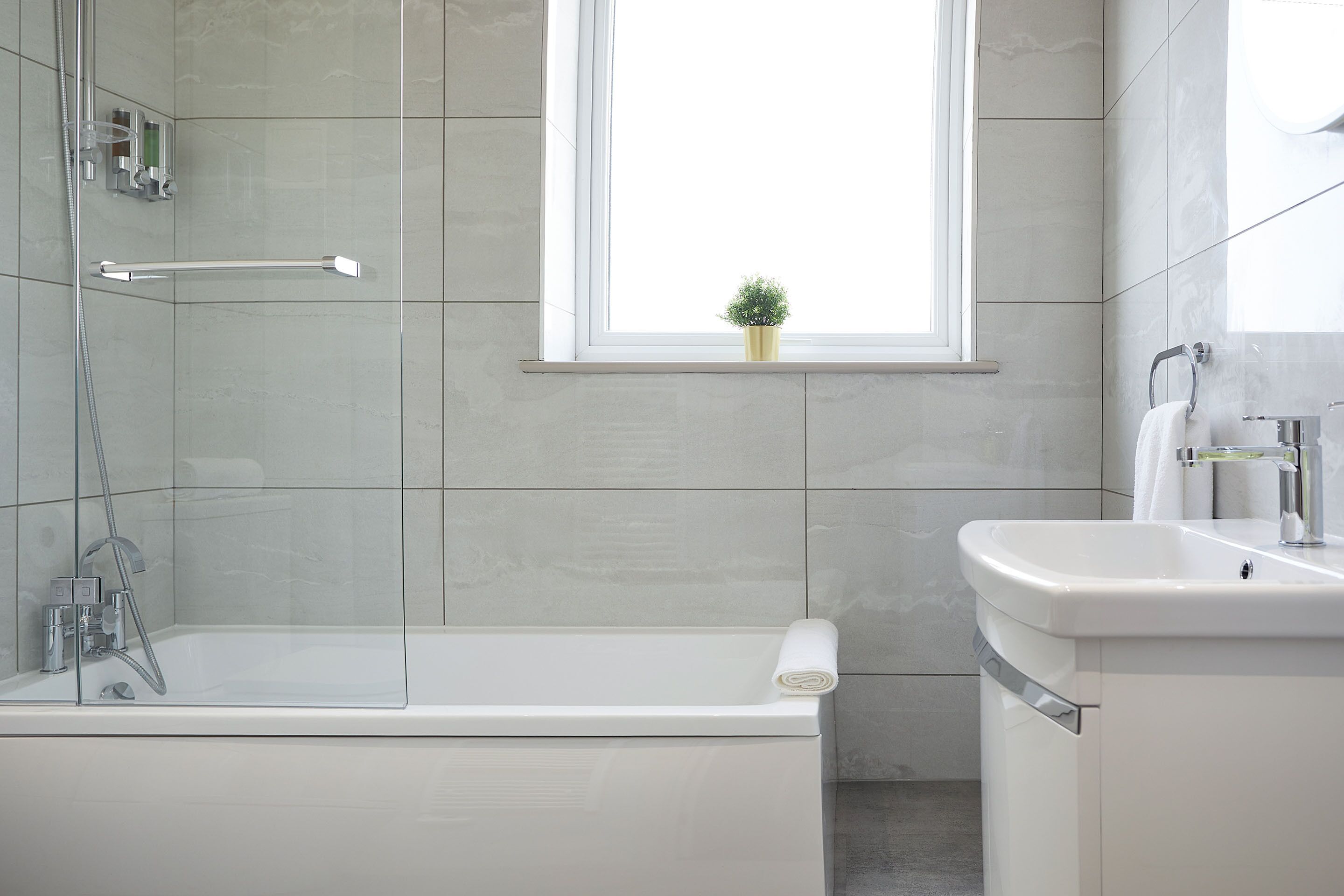 Une salle de bain moderne avec une douche à parois de verre, une fenêtre agrémentée d’une plante et un lavabo blanc.