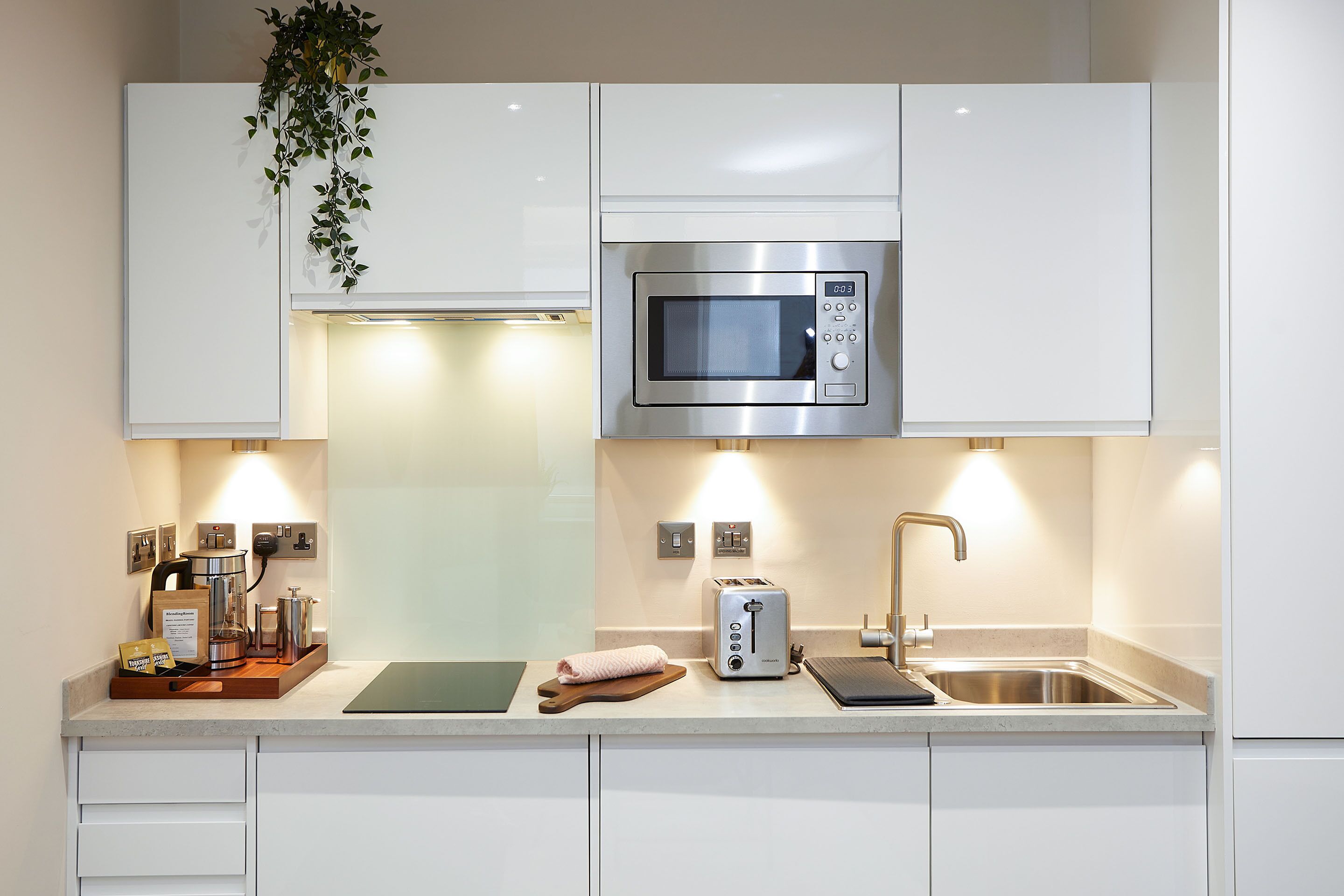 A modern kitchen with white cabinets, a stainless steel microwave, a toaster, and a sink.