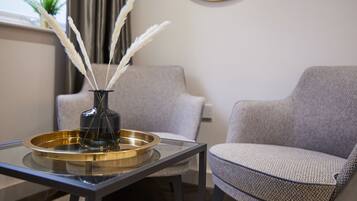 Un salon moderne avec une table basse en verre, un vase décoré de plumes blanches et deux fauteuils gris.