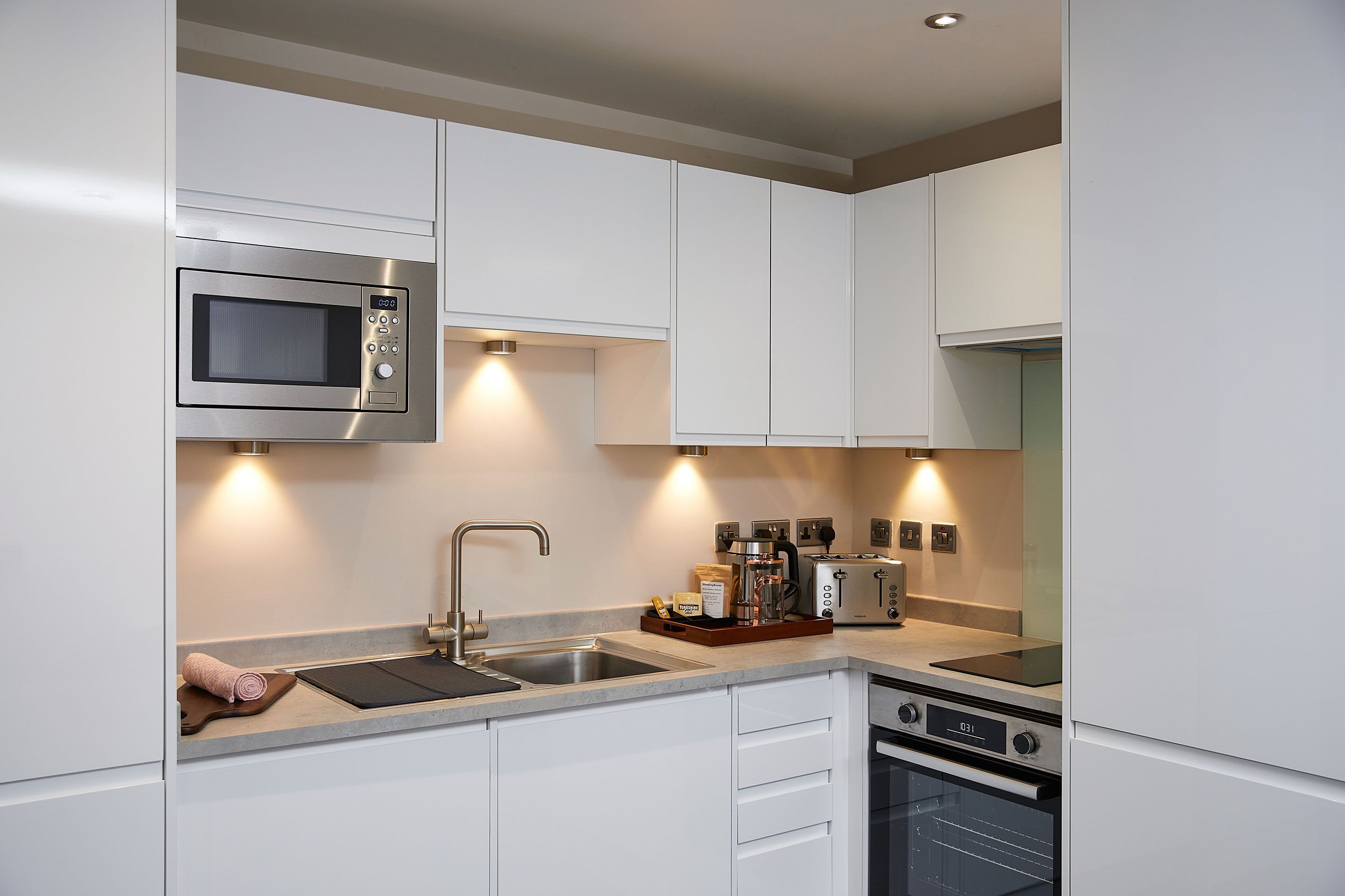 A modern kitchen with white cabinets, stainless steel appliances, a built-in oven, and a sink.