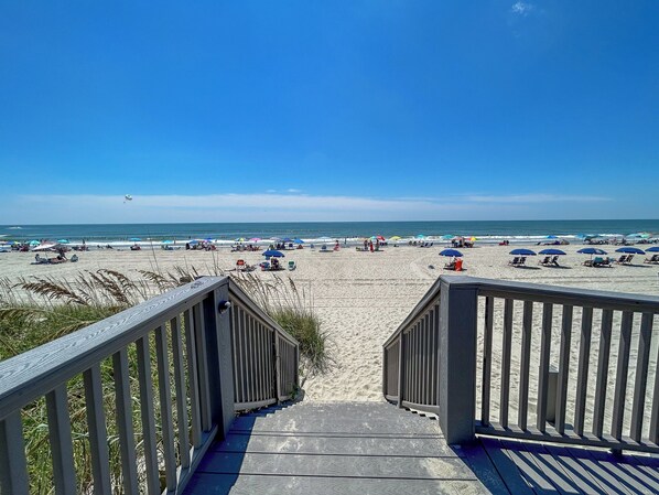 A wooden staircase leading to a beach with umbrellas and beach chairs.