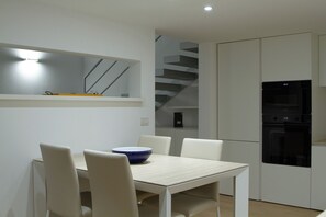 A modern kitchen with white cabinetry, a built-in oven, and a dining area with a table and chairs. - Charming loft in Moscova (Milano)
