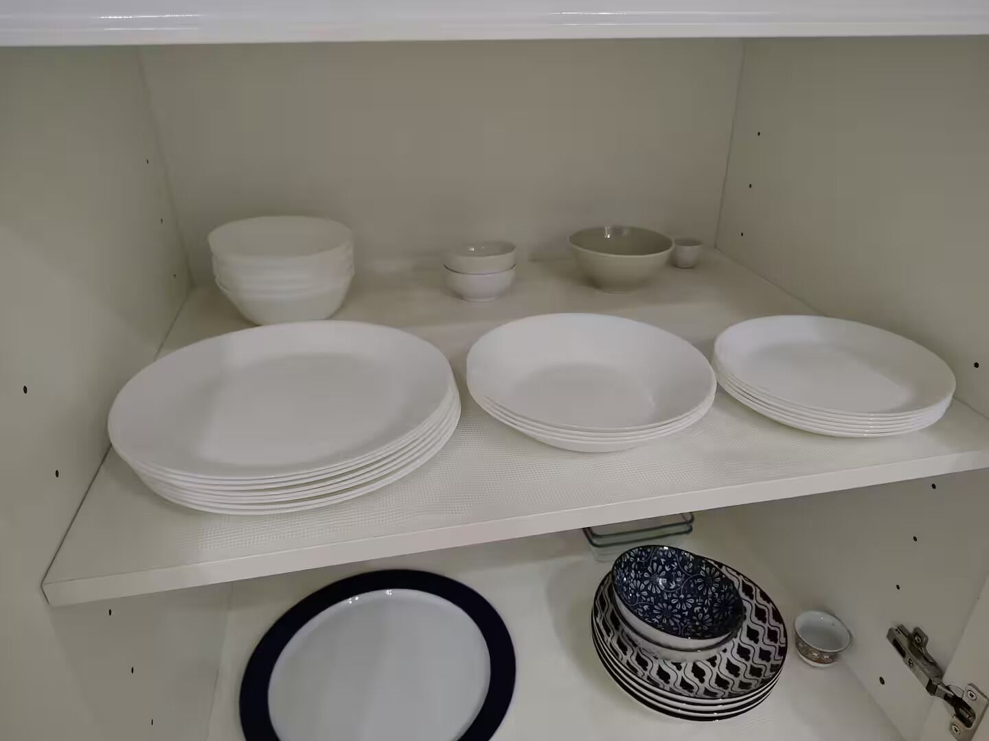 A white shelf with stacks of white plates, bowls, and a decorative bowl with a black rim.