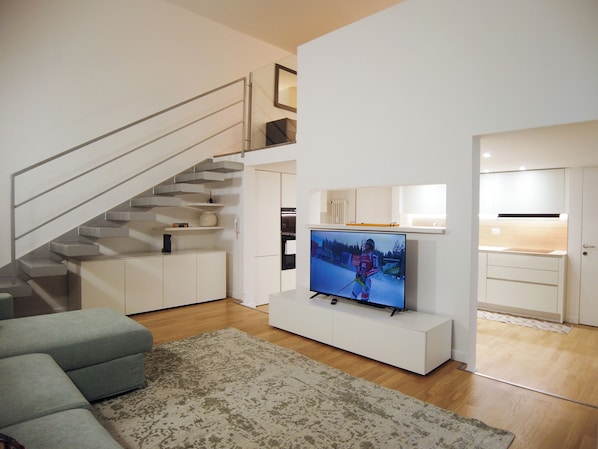 A modern living room with a flat-screen TV, a staircase, a kitchen area, and a seating area. - Charming loft in Moscova (Milano)