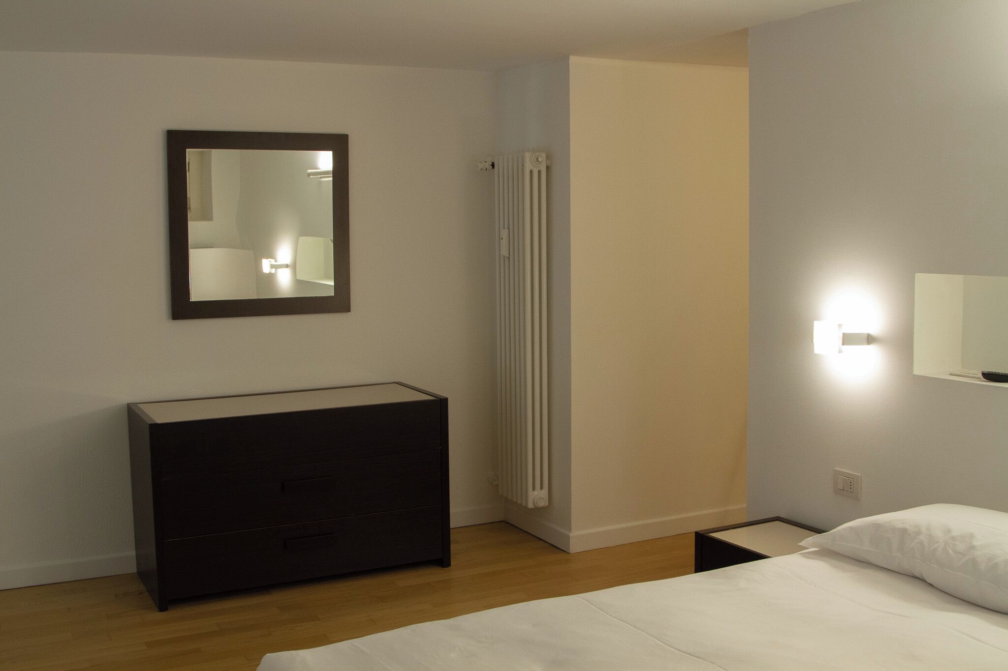 Une chambre à coucher avec un lit, une commode, un radiateur et un miroir.