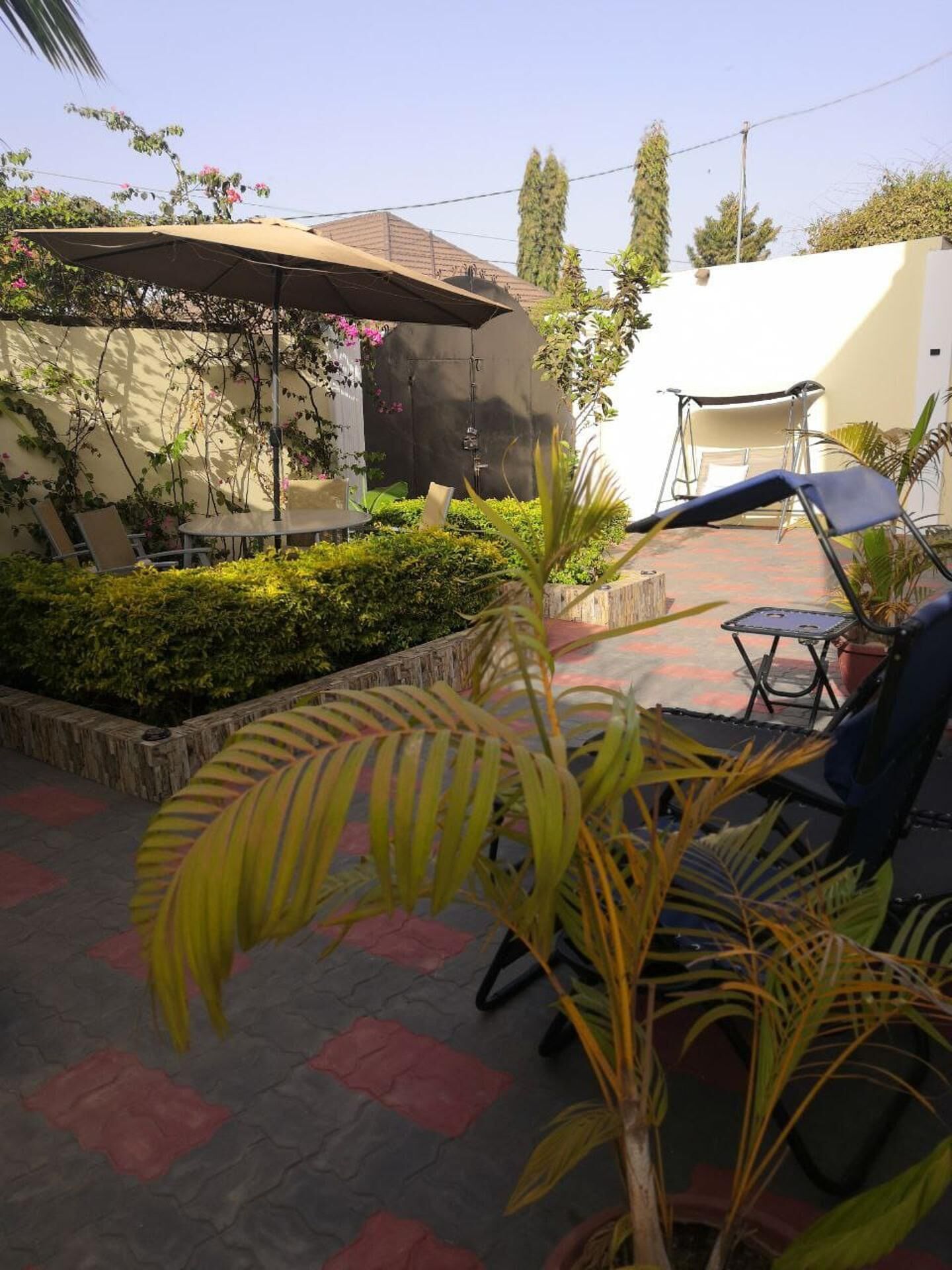Un espace extérieur aménagé en terrasse, avec une table et des chaises, entouré de verdure et surmonté d’une pergola.