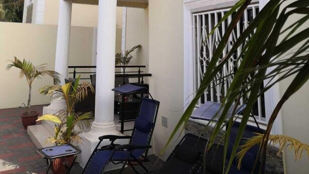 A two-story building with a balcony, outdoor seating area, and potted plants. - 4bed Villa Sleeps 8 - Wifi, Parking, Garden (Serrekunda)