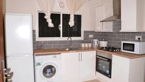 A compact kitchen with a washing machine, microwave, stove, and a sink. - 4bed Villa Sleeps 8 - Wifi, Parking, Garden (Serrekunda)