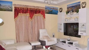 A living room with a sofa, two armchairs, a coffee table, and a TV stand with decorative items. - 4bed Villa Sleeps 8 - Wifi, Parking, Garden (Serrekunda)