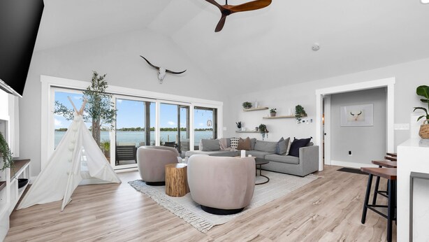 A spacious living room with a large window, a ceiling fan, and a cozy seating area. - Roxie's Modern Lake Front House on the water! (Russells Point)