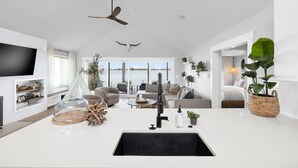 A modern living room with a large TV, a ceiling fan, and a view of the water. - Roxie's Modern Lake Front House on the water! (Russells Point)