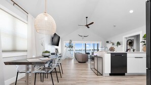 A modern kitchen with a dining area, large windows, and a ceiling fan. - Roxie's Modern Lake Front House on the water! (Russells Point)